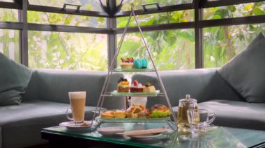 Tiered afternoon tea stand, elegance decadent pastries and delicate sandwiches, surrounded by lush tropical greenery in luxury hotel restaurant. Delicious sweet food.