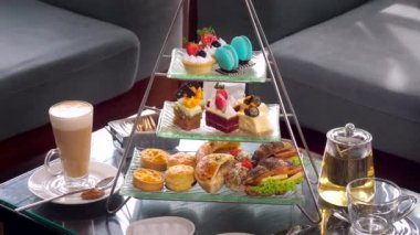 Renkli çay masası, cam çaydanlık, taze meyveli kekler ve bir dizi lezzetli tatlı, sandviçler ve lüks restoranda sıcak kahve. Lezzetli tatlı yemek..