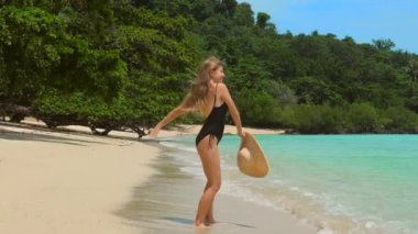 Tropik plajda zıplayan ve dans eden kadın. Neşeli bayan turist güneşli bir günde arka planda deniz manzarasıyla tatilin tadını çıkarıyor. Yaz tropik tatilleri. Yan görünüm.