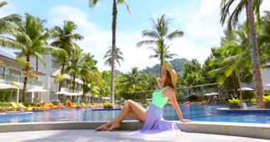 Göz kamaştırıcı genç kadın, ışıl ışıl yüzme havuzunun kenarında dinleniyor, sıcak güneşin tadını çıkarıyor ve bir dakikalık huzurun tadını çıkarıyor. Tayland tatili. Asya tatili.