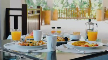 Variety of food on hotel breakfast buffet with tropical vibe. Fresh dishes and juices on table, palm trees in background. Luxury outdoor restaurant for vacation breakfast.