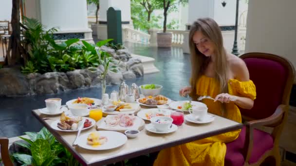 満足のいく朝食と豪華なホテルでおはようございます 若い笑顔の女性がソーセージ クロワッサンを食べ レストランで新鮮なジュースをすすります — ストック動画