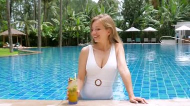 Genç bir kadın tropikal havuzda dinleniyor. Tatil ya da seyahat. Dişi gezgin, tropikal kokteyl içerken, yemyeşil palmiye ağaçlarıyla çevrili mavi yüzme havuzunda uzanıyor. Lüks ve huzurlu tatiller.