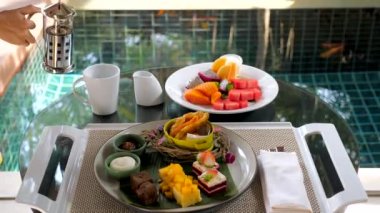 Lüks kahvaltı köşkü olan güzel tatil sabahları. Tropikal meyve ve kek tabakları, Fransız presinin elinden dökülen çay..