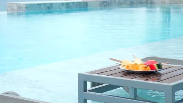 現代の高級リゾートのスイミングプールでスティック上のトロピカルフルーツプレート付きのテーブル 観光の概念 プールの横のテーブルの上に果物のボウル — ストック動画