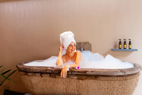 호텔의 목욕이요 아름다운 여자가 이색적 유기적 제품들이 거품으로 가득찬 욕조에서 — 스톡 사진