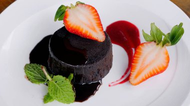 Lüks bir restoranda bir tabakta servis edilen naneli ve çilekli lezzetli çikolatalı pasta. Taze böğürtlen süslemeli bir dilim. Nane ve çilek soslu çikolatalı kek.