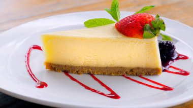 Meyve soslu ve taze çilekli bir dilim New York peynirli kekinin tadını çıkarın. Kremalı ve zengin tatlılar kafe veya restoranda beyaz bir tabakta servis edilir..