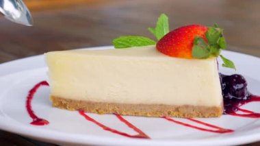 Nefis bir çilekli pastayı taze naneli ısıran bir kadının yakın plan görüntüsü. Lezzetli New York Cheesecake dilimi ve yanında taze çilek. Kremalı ve yumuşak tatlı, gurme lezzeti.
