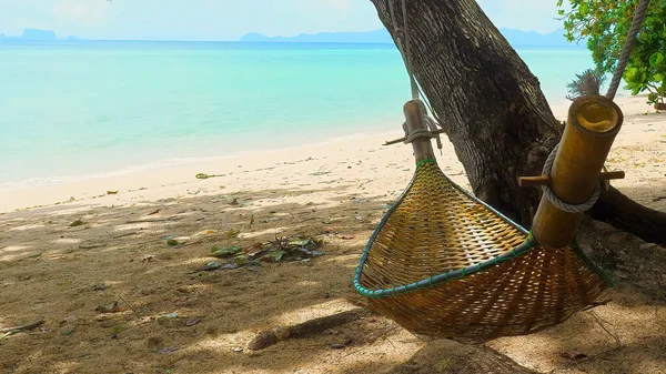 Hammock on summer sea beach with turquoise water. Straw hammock in the shadow of tropical trees on coastline. Tropical island with beautiful beach. Tourism, travel, vacation concept.