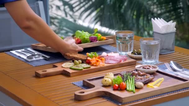 餐馆服务员在室外热带餐馆用餐 侍者把一块美味的木板放在桌上 餐厅的工作人员献上一顿精心准备的饭菜 — 图库视频影像