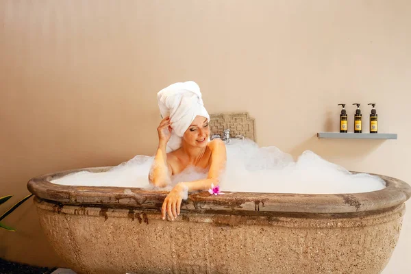 호텔에서 아름다운 수건을 머리에 거품이 욕조에서 긴장을 행복하게 미소를 짓는다 — 스톡 사진