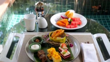 Yüzme havuzu ve tropik yeşillik olan lüks bir villada kahvaltı. Tabaklar dolusu egzotik meyve, kek ve tatlı. Tatil ve tatlı sabah yemeği