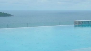 Mavi yüzme havuzuna damlayan yağmur damlaları güzel bir deniz arka planına sahiptir. Tropikal iklimde yağmur mevsiminde serin ve ferahlatıcı su yüzeyi dokusu.