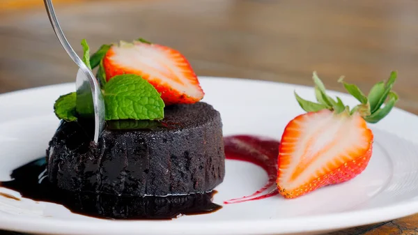 stock image Taking a bite of moist and tasty chocolate cake with fork. Delicious chocolate cake slice with mint and strawberries. Closeup of homemade pastry with dark cocoa, fresh berries and sweet cream.