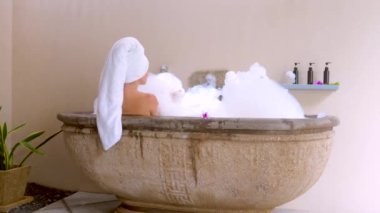 Lüks banyo banyosu sırasında kadının yavaş çekimde köpük üflemesi. Seksi kız sabun köpüğü banyosuyla spa terapisini seviyor. Şehvetli bir kadın, kendine bakması ve rahatlaması için zaman ayırır. Arka plan
