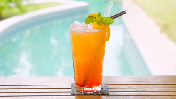 Close up of a refreshing orange drink with straw and mint leaf, perfect for a hot summer day at the pool. Relax in the background of the beautiful blue sea and enjoy a cold cocktail.