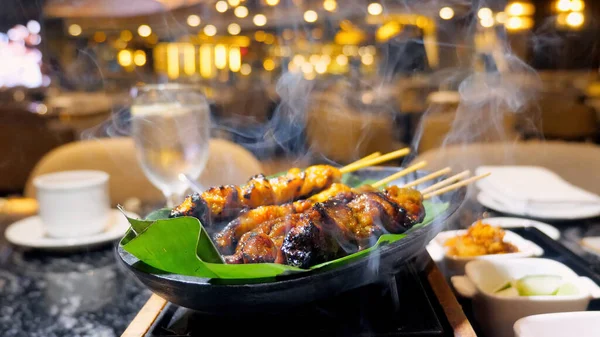 stock image Satay chicken skewers cooked on the grill with smoke. Delicious Malaysian dish in a modern luxury restaurant. Skewered chicken grilled to perfection over charcoal. Fine dining food.