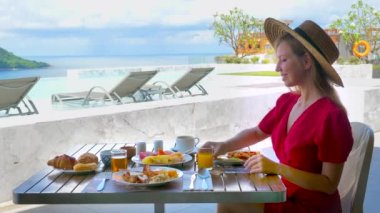 Yaz tatilinde olan genç bir kadın tropikal meyvelerle kahvaltı yapıyor, deniz manzaralı lüks bir otel terasında portakal suyu içiyor..