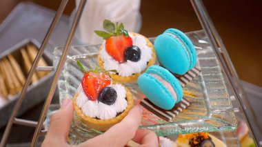 Kadın eli, restorandaki geleneksel ikindi çay standından tatlı bir tart alır. Renkli lezzetli tatlı yiyecekler..