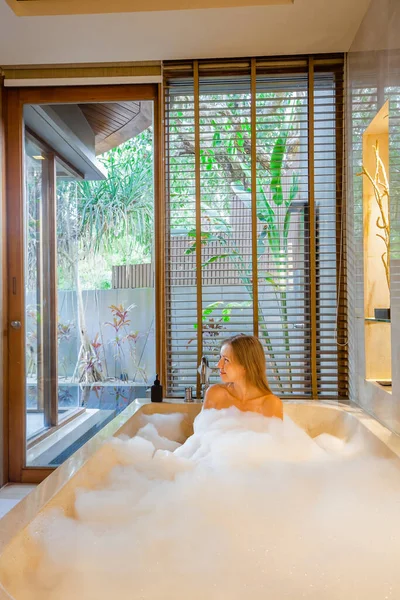 在奢华的热带别墅里 一个漂亮的裸体女人正在一个现代化的浴室里 在一个充满泡沫的浴缸里享受着放松的浸泡 温泉和放松 美容美发 度假概念 — 图库照片