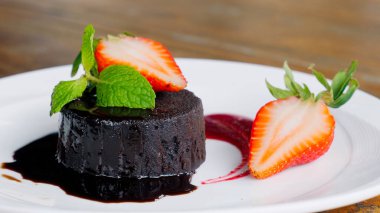 Siyah tabakta servis edilen taze çilekli lezzetli çikolatalı pasta. Lokantada kakao jöleli ve naneli ev yapımı çikolatalı pasta..