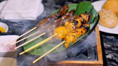 Muz yaprağında soğan ve sosla servis edilen ahşap şişler üzerinde kızartılmış tavuk satay. Lezzetli Malay mutfağı kömür ızgarasında dumanla pişirilir. Lüks modern restoranda lezzetli yemekler yiyin..