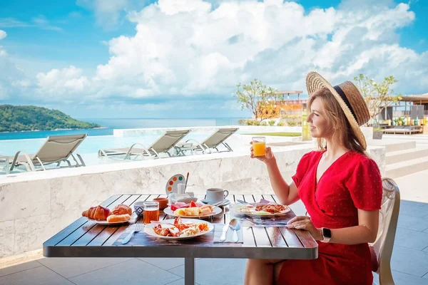 stock image Young woman on summer vacation enjoying breakfast with tropical fruits, drinking orange juice on a luxury hotel resort terrace overlooking the sea.