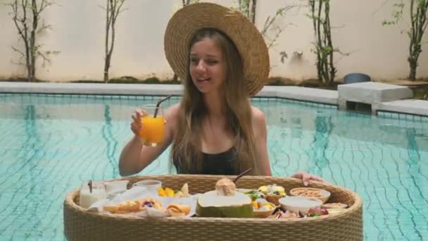 在热带别墅的游泳池里 这位年轻的女士享受着新鲜的橙汁 游客在度假 放松在豪华度假胜地 暑假的快乐 — 图库视频影像