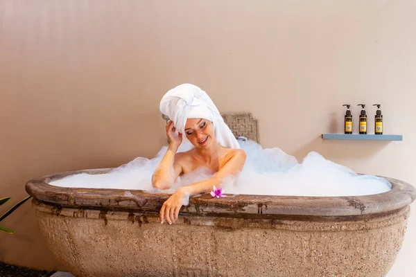 호텔의 목욕이요 아름다운 여자가 이색적 유기적 제품들이 거품으로 가득찬 욕조에서 — 스톡 사진