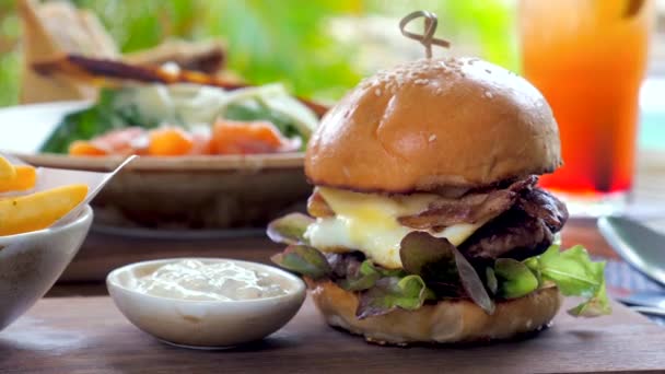 在室外餐馆里享用的美味牛肉汉堡的包装 烤过的馅饼上有奶酪 西红柿和洋葱 用新鲜的面包包着吃 — 图库视频影像