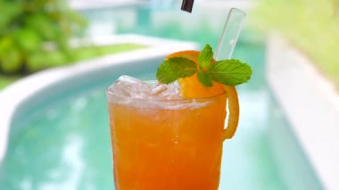 Adam güzel dekore edilmiş portakal suyuna, havuz kenarında meyve ve nane aromalı bir pipet yerleştiriyor. Rahatlayın ve lüks bir tatil köyünde tropikal bir tatil yapın..