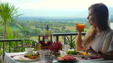Gezgin taze portakal suyu yudumluyor, otelde lezzetli bir kahvaltı yapıyor. Yemek dolu bir masa, güzel yeşil vadi manzarası, mükemmel bir yaz tatili. Seyahat, tatil ve tatil ile ilgili konsept.