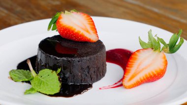 Taze böğürtlenlerle süslenmiş beyaz bir tabakta kremalı çikolatalı mus. Lokantada çilek ve nane yaprağı ile servis edilen gurme tatlıları..