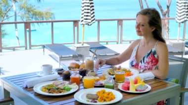 Pazar brunch 'ında kahve içen genç bir kadın oteldeki açık hava restoranında ya da tatil sırasında Tayland, Phuket' te tatil yapıyor. Mavi deniz arka planı. Kahvaltı, kafede öğle yemeği..