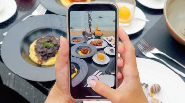 Açık hava tropikal bir restoranda akşam yemeğinin fotoğrafını çekmek için akıllı telefon kullanan bir kadının elleri. Lezzetli yemekleri moda bir uygulama ile yakalıyor..