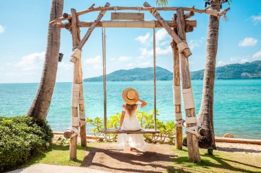 Yaz yolculuğu konsepti. Hasır şapkalı kadın okyanusa tepeden bakan deniz manzaralı mutluluk ve özgürlükle sallanıyor. Mükemmel bir tatil kaçışı..