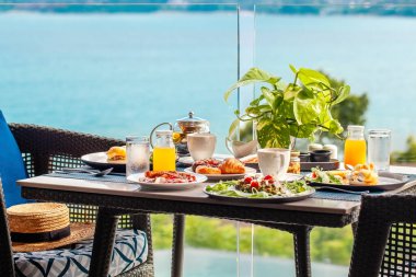 Deniz kenarında romantik bir kahvaltı masası, içinde yumurta, hamur işi, kahve ve portakal suyu gibi lezzetli yiyecekler var. Yaz tatili ya da hafta sonu kaçamağı için mükemmel..