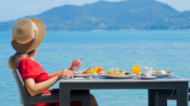 Tatilde olan genç bir kadın lüks bir restoranda sağlıklı yiyeceklerle birlikte sabah yemeğinin tadını çıkarıyor. Tayland tatili.