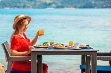 Deniz manzaralı lüks bir otelde dinlenen bir kadın güne deniz kenarındaki bir restoranda sağlıklı bir kahvaltıyla başlıyor. Phuket adasının tropik cenneti, Tayland tatili.