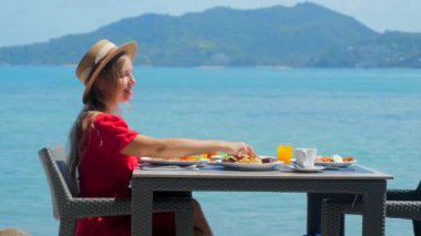 Deniz manzaralı lüks bir otelde dinlenen bir kadın güne deniz kenarındaki bir restoranda sağlıklı bir kahvaltıyla başlıyor. Phuket adasının tropik cenneti, Tayland tatili.