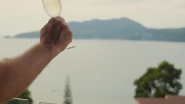 Adamın biri çarpıcı bir günbatımı deniz manzarasına karşı şampanya kadehini kaldırıyor. Erkekler tatil, rahatlama ve lüks tatil beldelerinde lüksü kutlarlar..