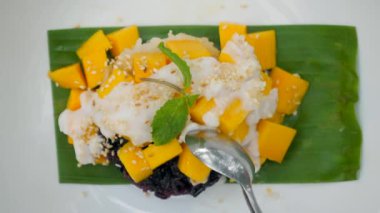 Kadın, kaşık kaşık mango yapışkan pirinç yiyor. Taze mango, glutinous pilavı ve cömert hindistan cevizi sütü ile tatlı ve yapışkan tatlı manzaralı temalı Tayland mutfağı. Kapat..