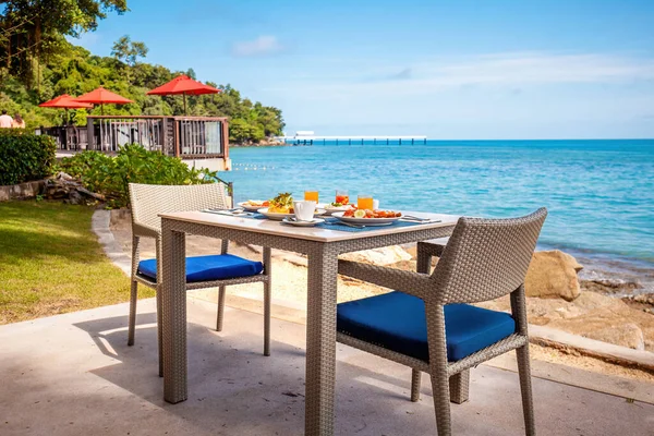 Breakfast table full of food at seaside restaurant, with sea view. Summer dinner at a beachfront restaurant in luxury hotel. Concept of travel, holidays, weekend, tropical vacation in resort.