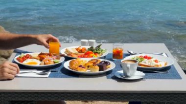 Tropikal bir otelde lezzetli bir kahvaltı yapın. Lüks bir sahil köşkünde açık büfede portakal suyu içen bir adam. Sahildeki bir restoranda yemek yiyorum.