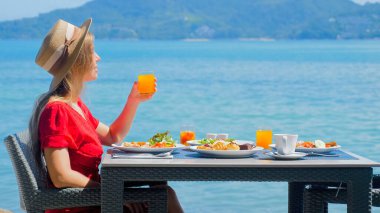 Lüks bir otelde dinlenen bir kadın, deniz manzaralı bir kahvaltı. Turkuaz okyanusa bakan tatilci kız. Tropikal tatil merkezleri..