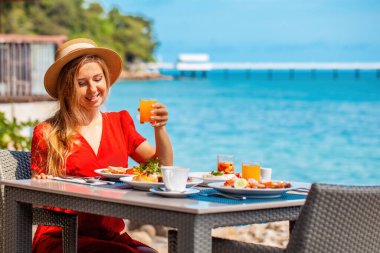 Genç bir kadın, deniz manzaralı lüks bir tatil köyünde açık büfe kahvaltıdan hoşlanıyor. Yaz tatilindeki nüfuzlu kız, sahil restoranında lezzetli yemekler yiyor. Yaz tatili.