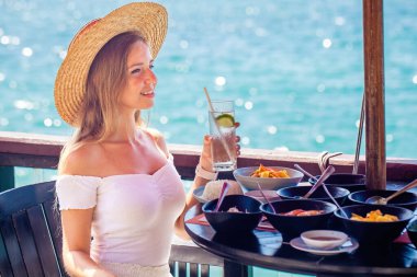 Yaz tatilindeki genç bir kadın deniz manzaralı lüks bir otel odasında lezzetli bir kahvaltı yapıyor. Kız yaz tatilinin tadını çıkarıyor..
