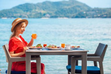 Deniz manzaralı lüks bir otelde dinlenen bir kadın güne deniz kenarındaki bir restoranda sağlıklı bir kahvaltıyla başlıyor. Phuket adasının tropik cenneti, Tayland tatili.