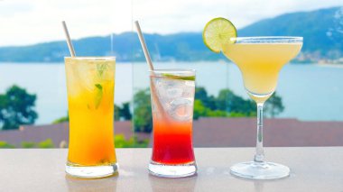 Otelin yüzme havuzunun yanında deniz manzaralı tropikal meyve kokteylleri. Üç renkli bardakta harmanlanmış içecek. Yaz tatili için mükemmel..
